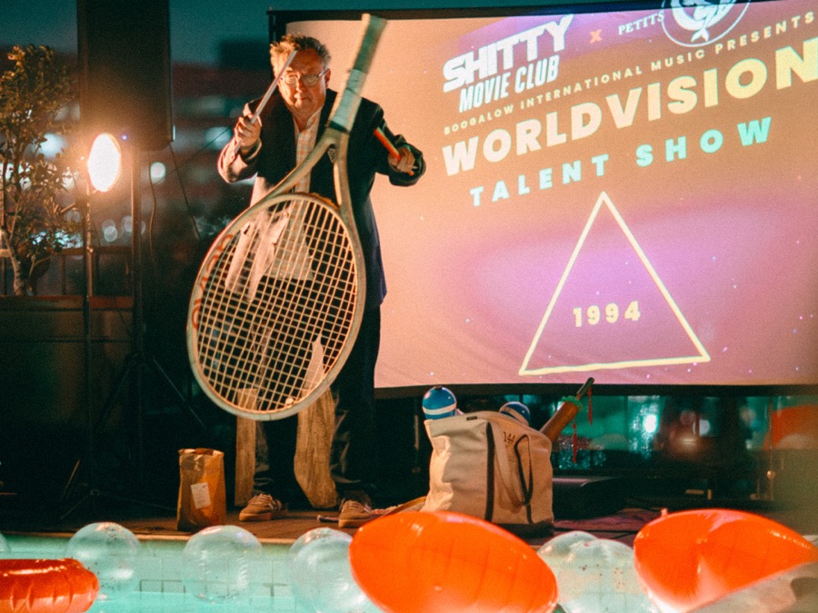 A host with a giant tennis racket in front of the screen